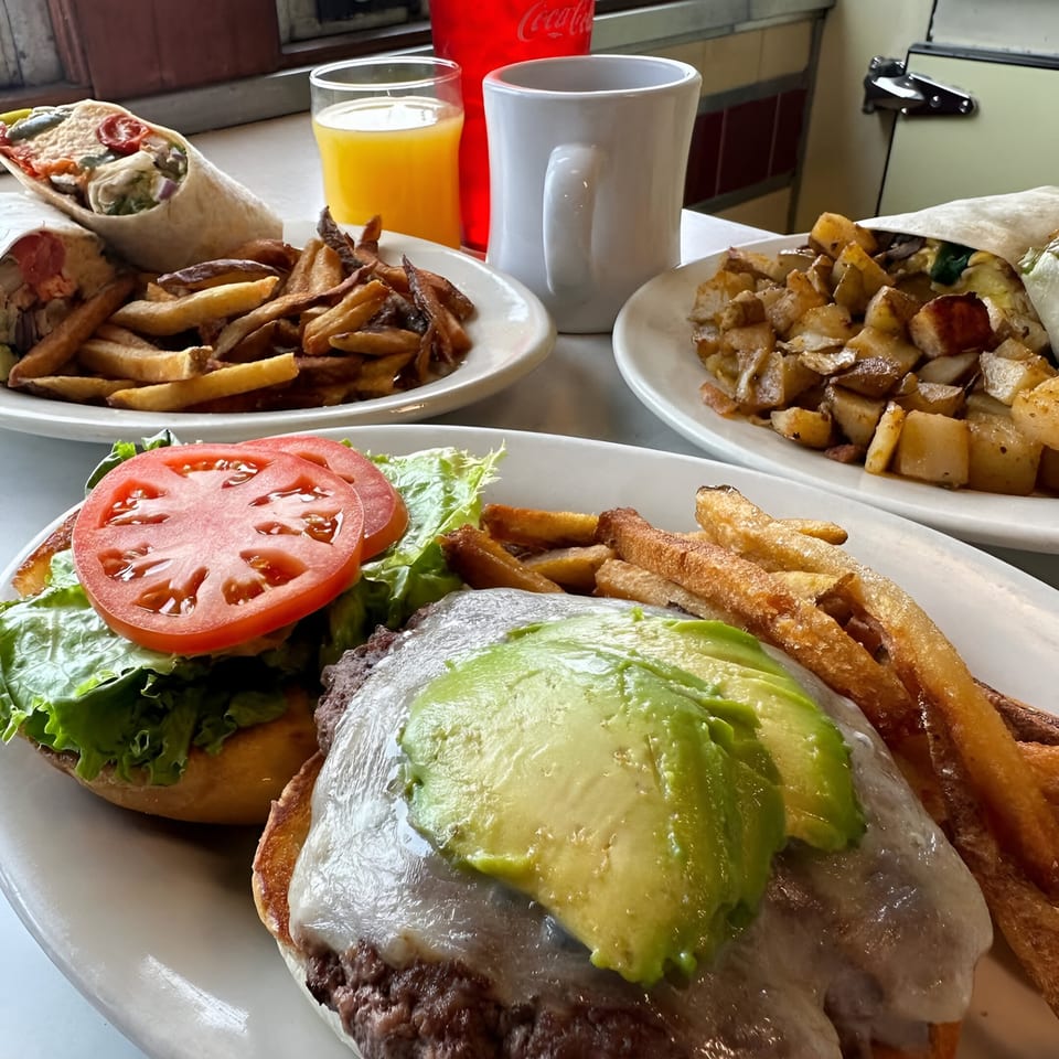 A diner table with a burger, fries, wraps, home fries, orange juice, and coffee.