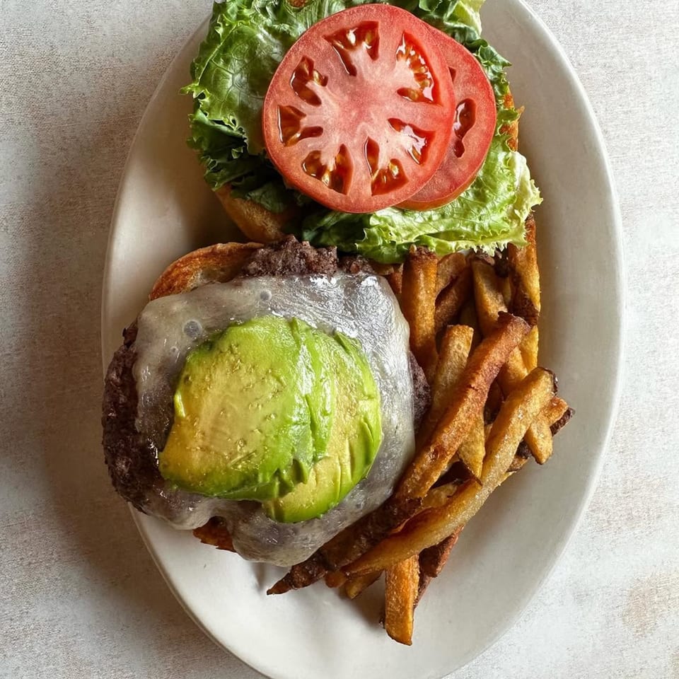 A Parkway Diner burger with avocado, melted cheese, lettuce, tomato, and a side of fries.