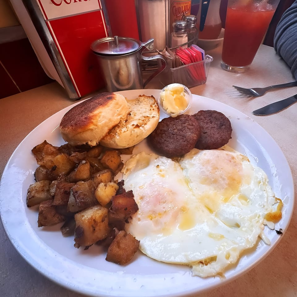 A Parkway Diner breakfast plate with fried eggs, sausage patties, home fries, and a toasted English muffin.