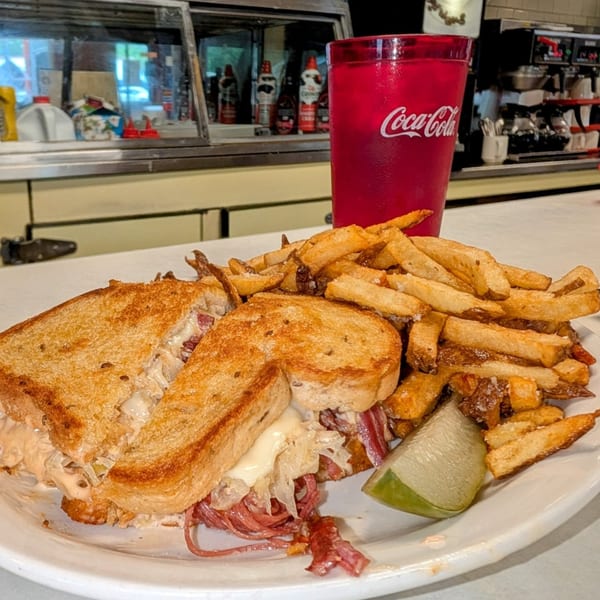 A Parkway Diner Reuben sandwich with fries and a lime wedge, next to a red Coca-Cola cup.