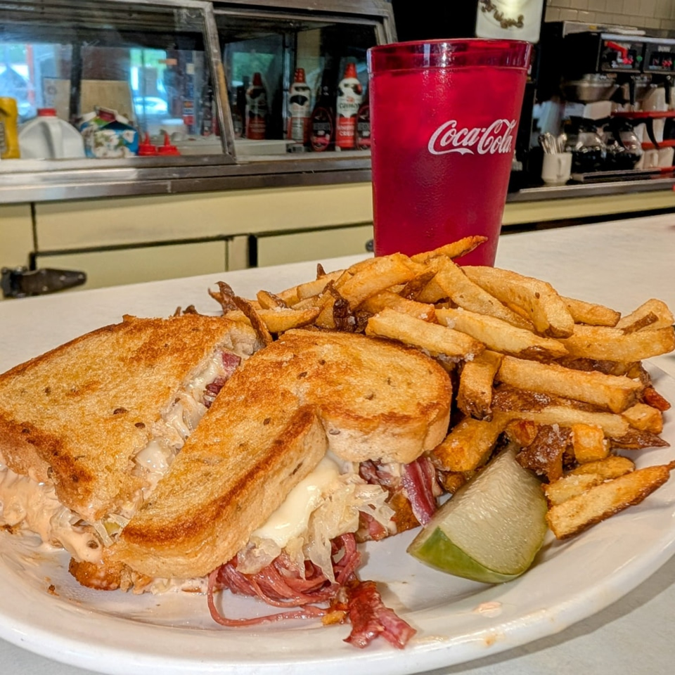 A Parkway Diner Reuben sandwich with fries and a lime wedge, next to a red Coca-Cola cup.