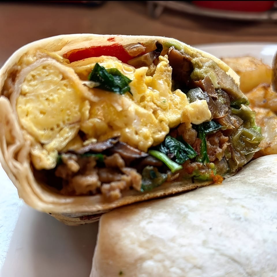 Close-up of a Parkway Diner breakfast burrito, revealing scrambled eggs, spinach, and mushrooms.
