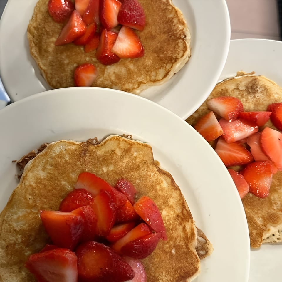 Three plates of golden-brown pancakes topped with fresh, sliced strawberries at Parkway Diner.